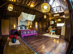 A rustic wooden room with a bed, a dining table, and a kitchen area. - Easy Surf Dacha (Pererenan)