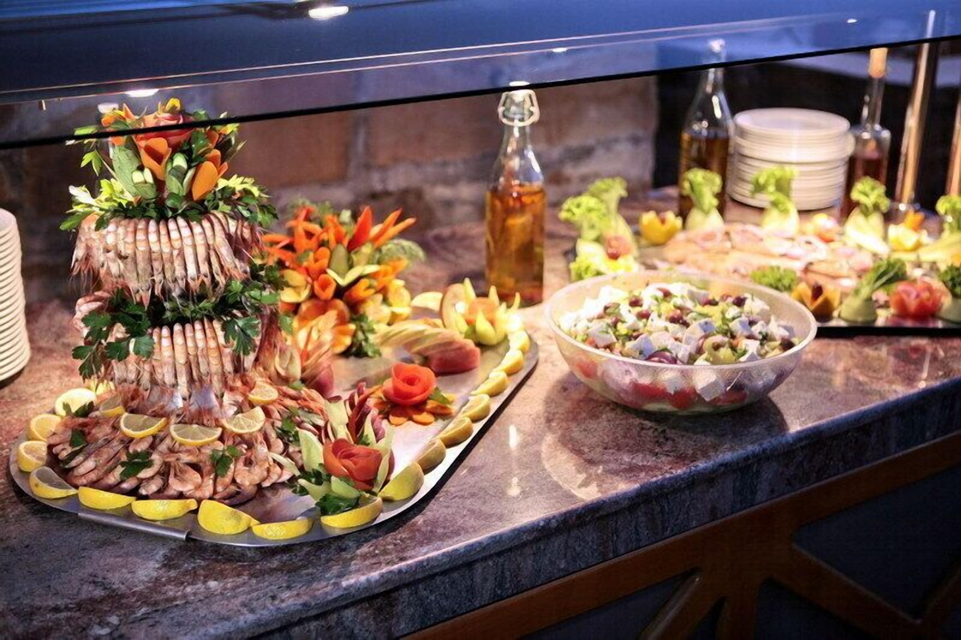Una mesa de buffet con diferentes alimentos, incluyendo un centro de camarones y vegetales, y un tazón de ensalada.