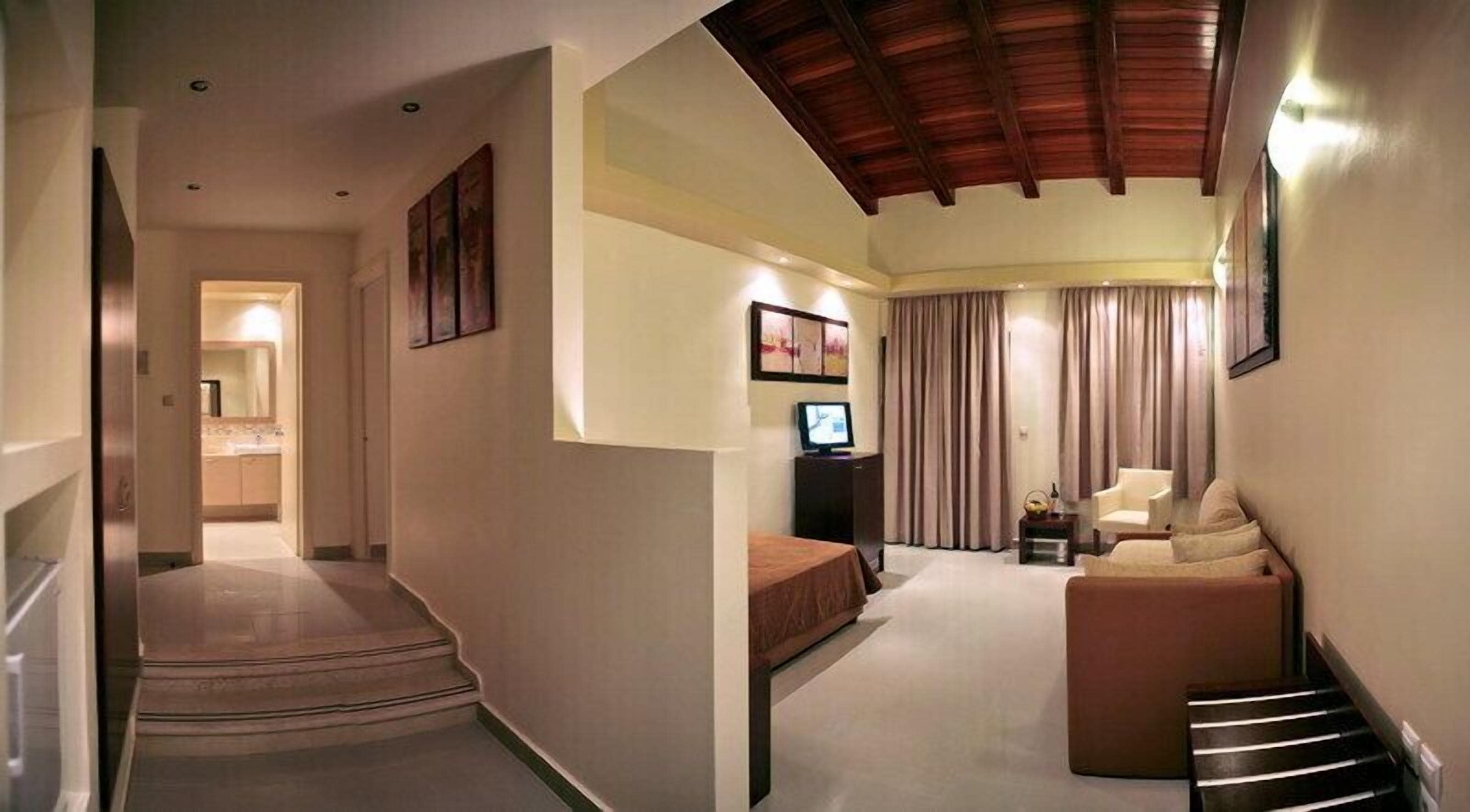 A hotel room with a staircase leading to a bathroom, a living area with a sofa and curtains, and a TV on a stand.