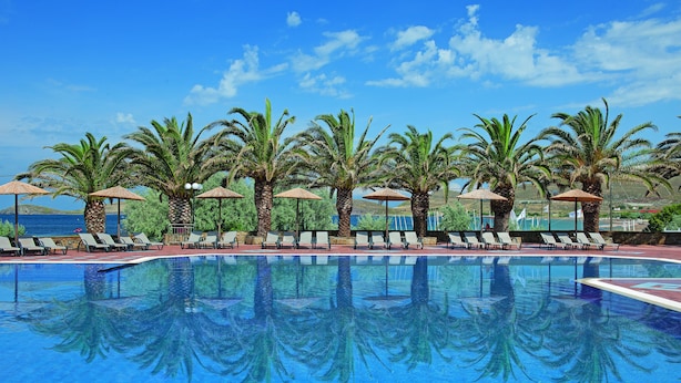A pool with palm trees and lounge chairs, surrounded by a clear blue sky. - Lemnos Village Resort (Lemnos)