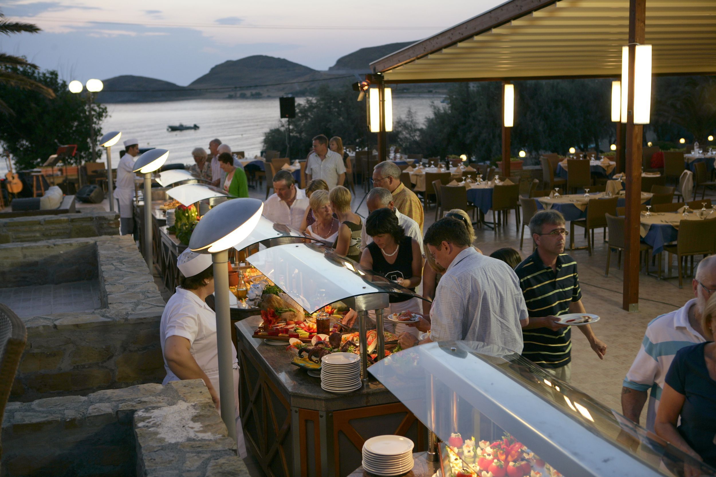 Un espace de restauration en plein air avec un buffet, offrant une vue sur un plan d’eau et des collines.