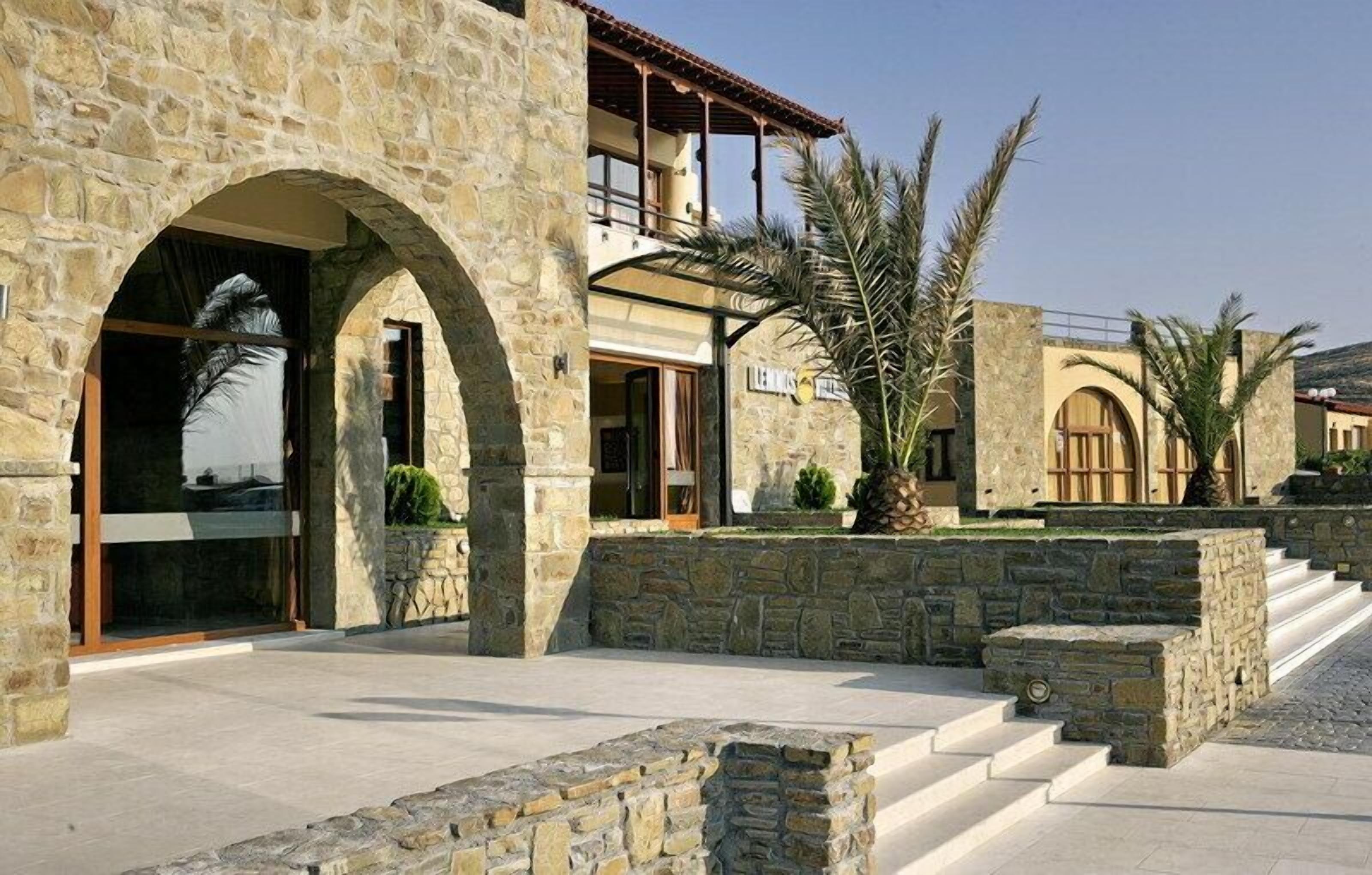 A stone building with arched entrances, a balcony, and palm trees.