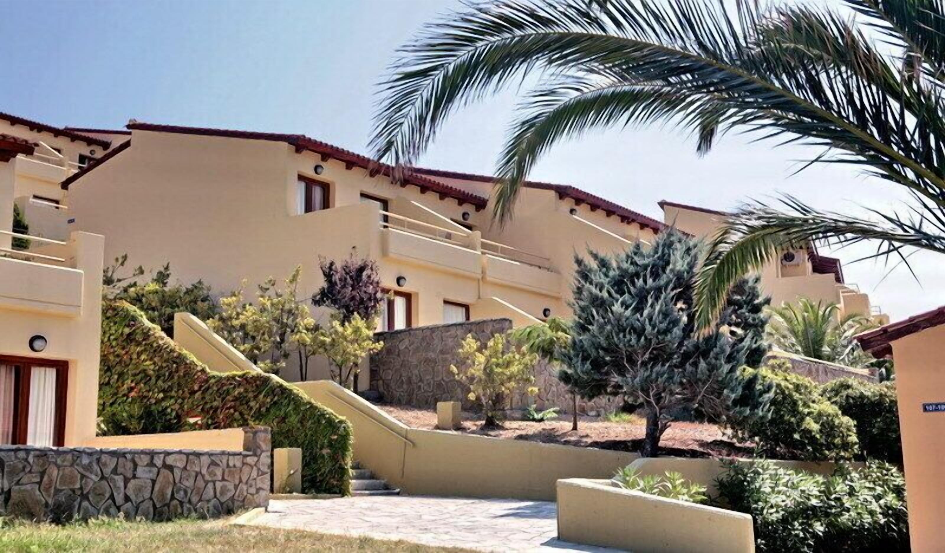 Un edificio de varios pisos con fachada color beige, escalones de piedra y una palmera.