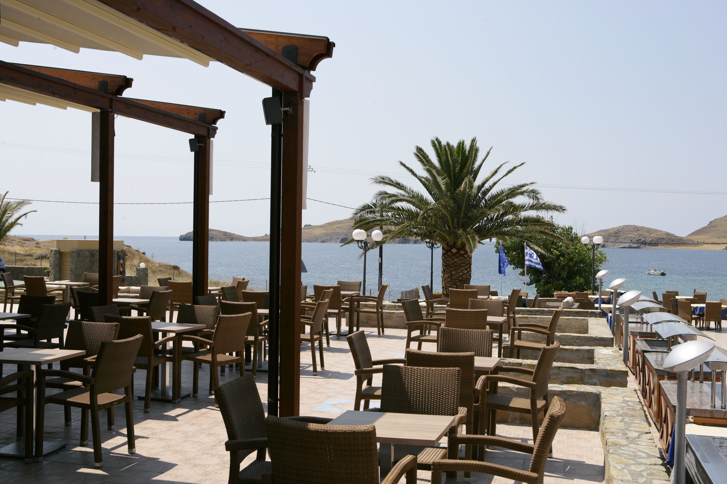 An outdoor cafe with tables and chairs, overlooking a body of water and hills.