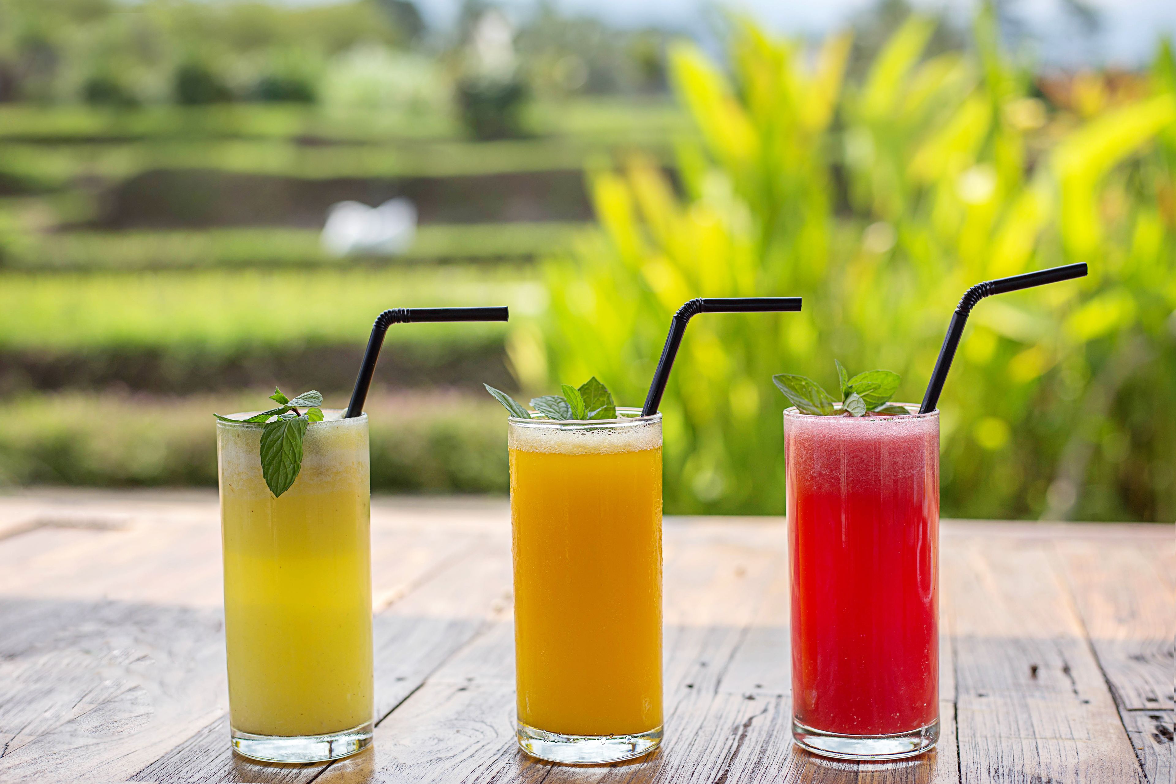 Three glasses of beverages on a wooden table with a blurred green background.
