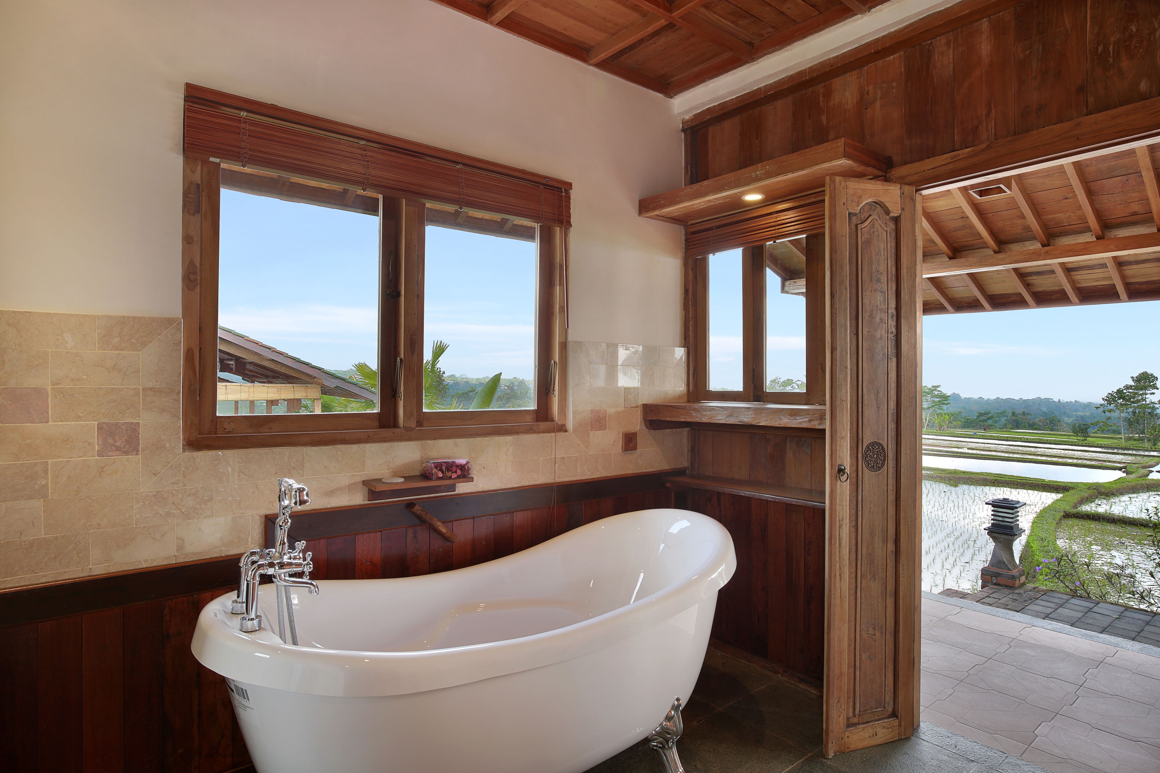 A bathroom with a freestanding bathtub, wooden paneling, and large windows offering a view of a landscaped area.