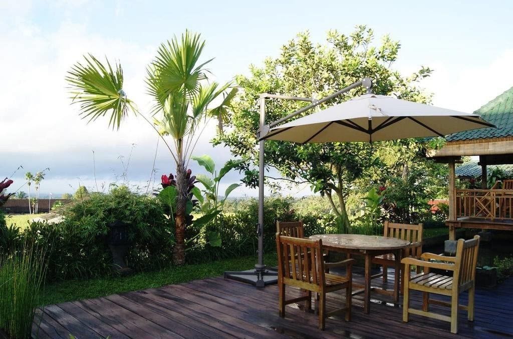 An outdoor patio with a wooden table and chairs, a metal umbrella, and lush greenery.