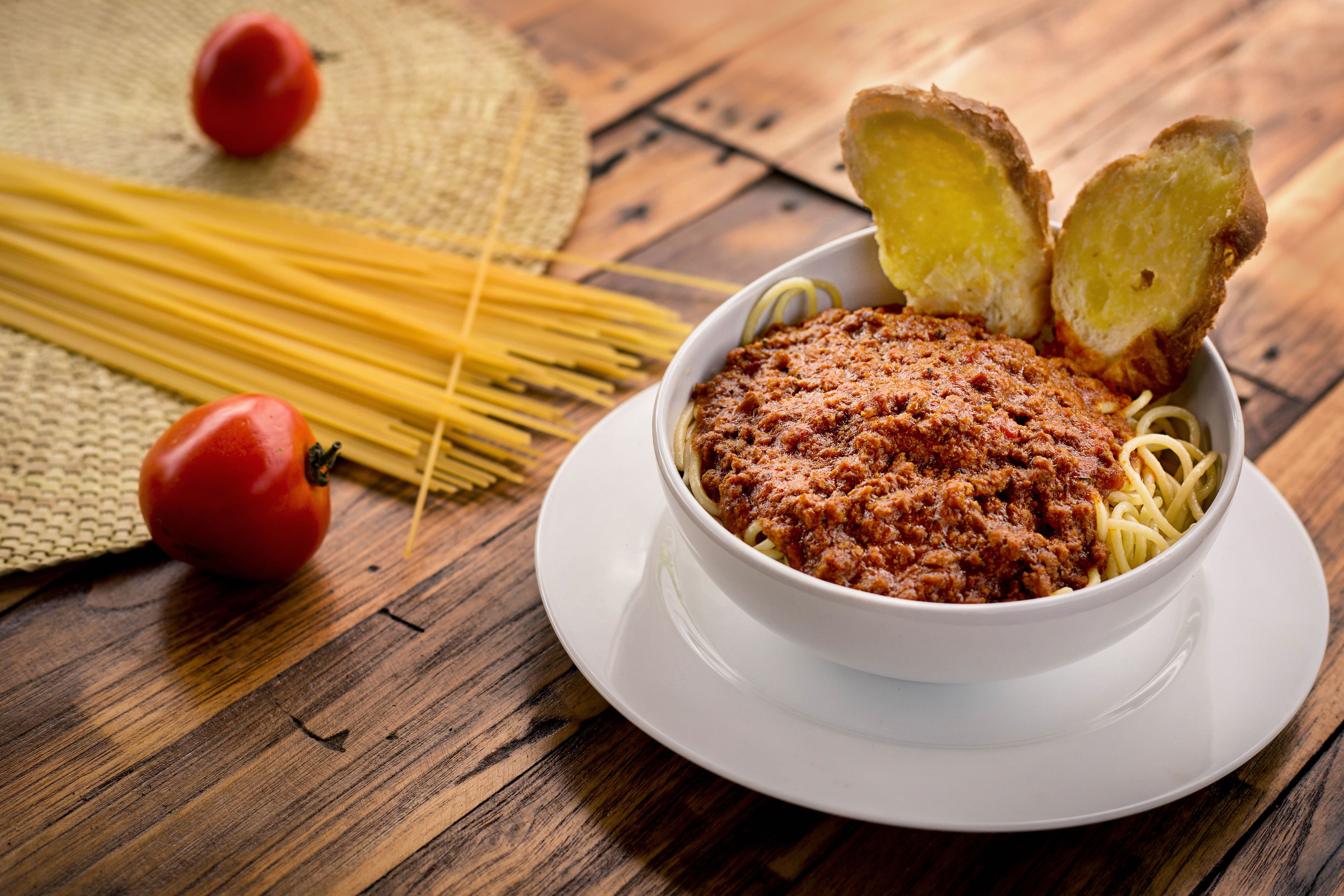 Uma tigela de espaguete com molho de tomate e palitos de pão em uma mesa de madeira.