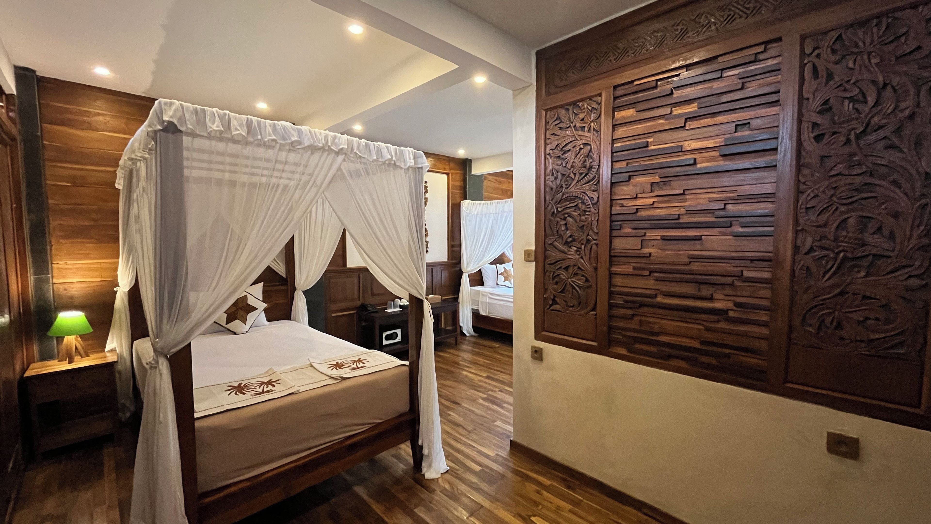 Una cama con dosel y columnas, paneles de madera en las paredes y una mesita de noche con lámpara.