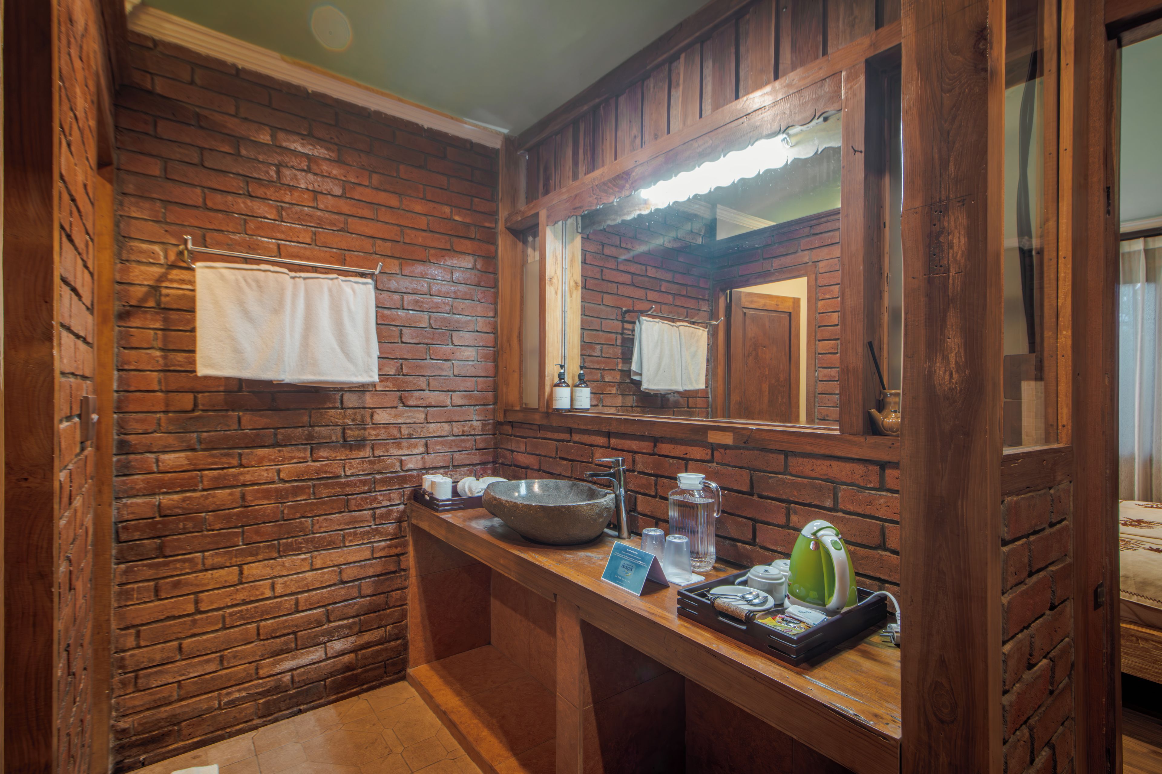 Un bagno con parete in mattoni, mobile lavabo in legno, un ampio lavabo e uno specchio.