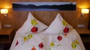 A hotel room with two beds, each with a pillow featuring a floral design. There is a large framed picture above the beds depicting a landscape. - Gästehaus Café Heck (Titisee-Neustadt)