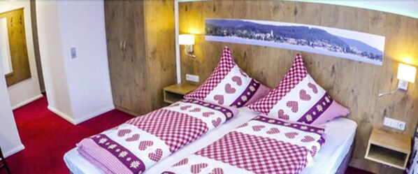 Habitación de hotel con cabecera de madera, dos mesitas de noche con lámparas, alfombra roja y una cama con colcha a cuadros.