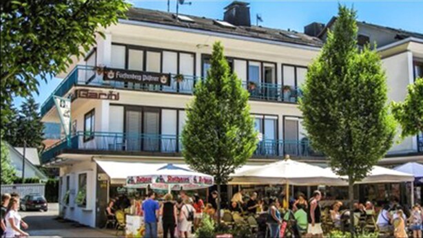 A building with multiple balconies and a cafe with outdoor seating. - Gästehaus Café Heck (Titisee-Neustadt)
