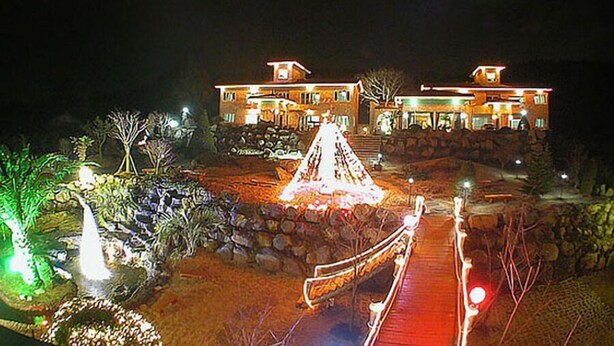 A large, well-lit building with a prominent entrance and a bridge leading to it. - Palace in the Forest Pension (Seogwipo)