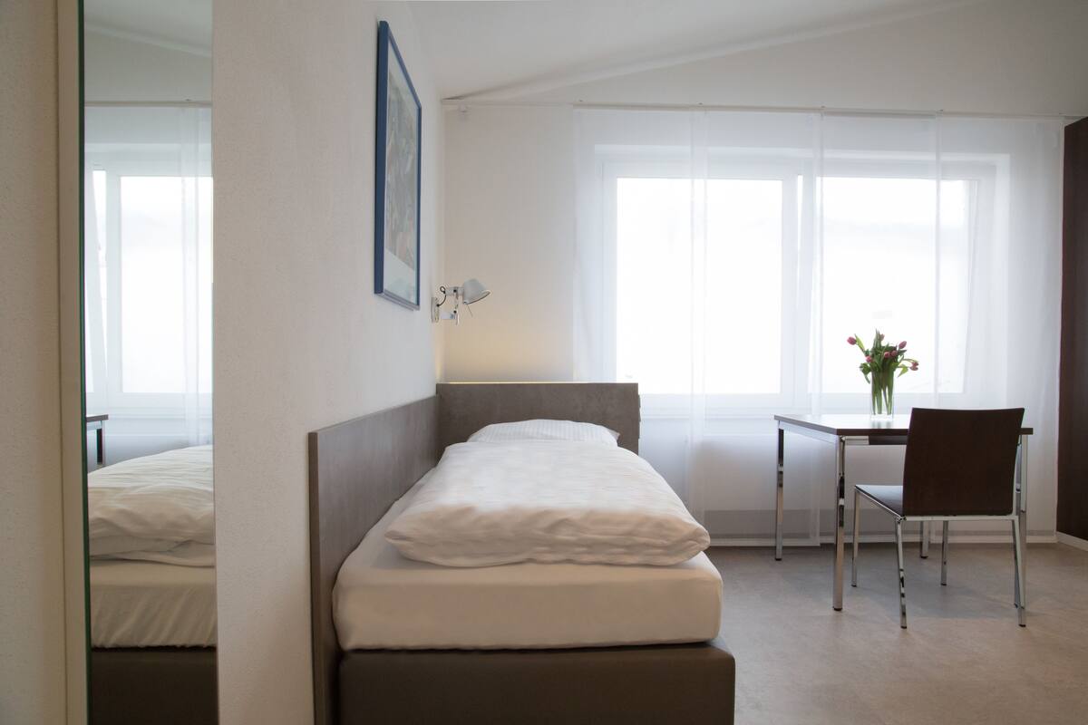 A hotel room with a bed, a desk, a chair, and a window with curtains.