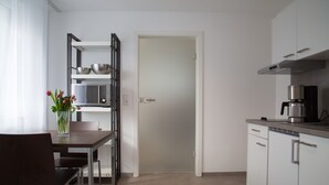 A modern kitchen with white cabinets, a coffee machine, and a dining area with a table and chairs. - Apartmenthaus Renz (Aalen)