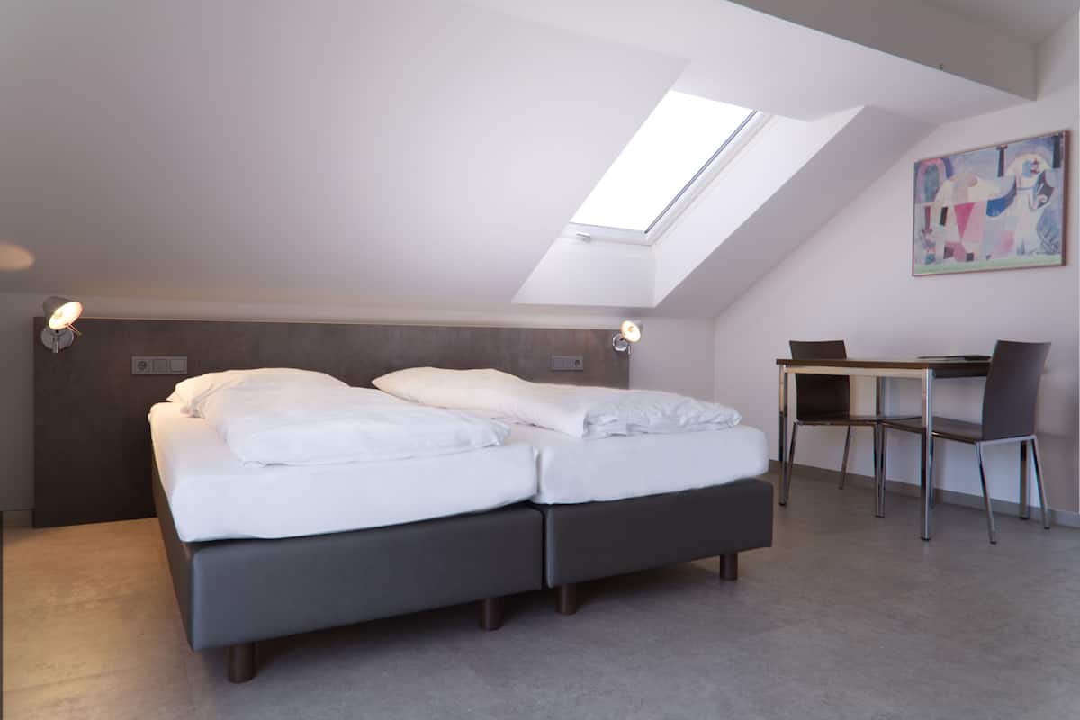A bedroom with a skylight, a bed, a desk, and a chair.