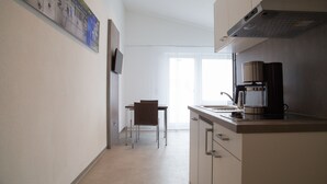 A modern kitchen with a coffee machine, a dining area with a chair, and a large window. - Apartmenthaus Renz (Aalen)
