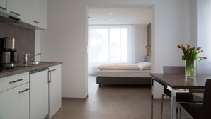A modern kitchen with white cabinets, a coffee machine, and a dining area with a table and chairs. - Apartmenthaus Renz (Aalen)