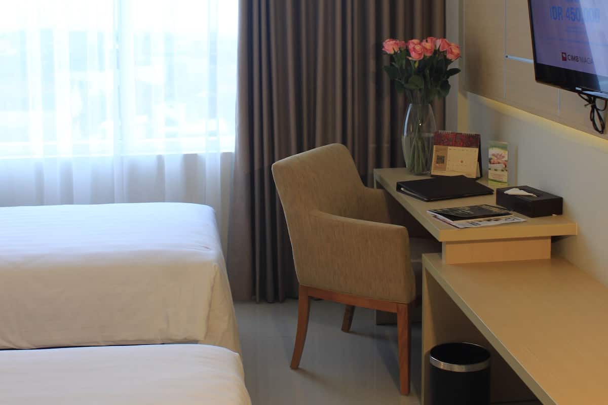 Habitació d'hotel amb dos llits, una escriptori amb un monitor d'ordinador, una cadira, un ram de flors i un cubell de paper.