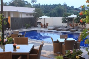 A poolside area with lounge chairs, tables, and umbrellas. - Horison Hotel Sukabumi (Sukabumi)