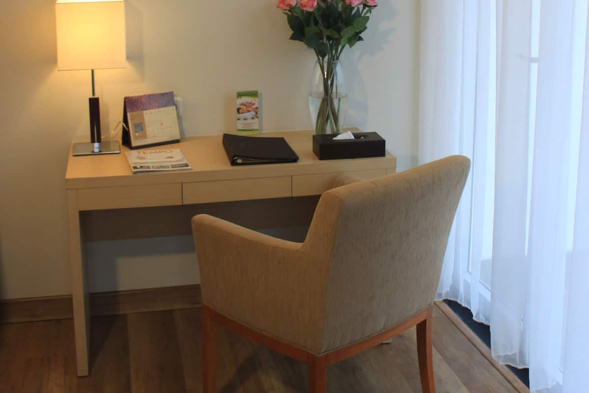 Habitació d'hotel amb escriptori de fusta, una làmpada, un ram de flors i una cadira.
