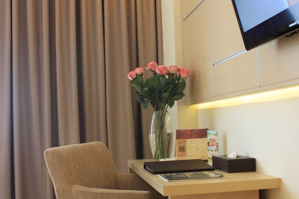 Habitació d'hotel amb escriptori de fusta, una cadira, un ram de flors, televisió de pantalla plana penjada a la paret i una cortina.