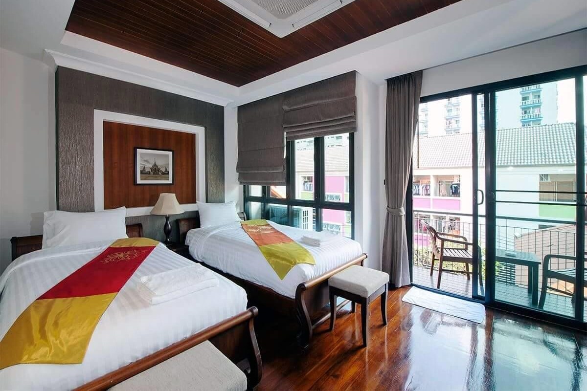 A hotel room with two beds, a wooden ceiling, a large window, and a balcony with chairs.