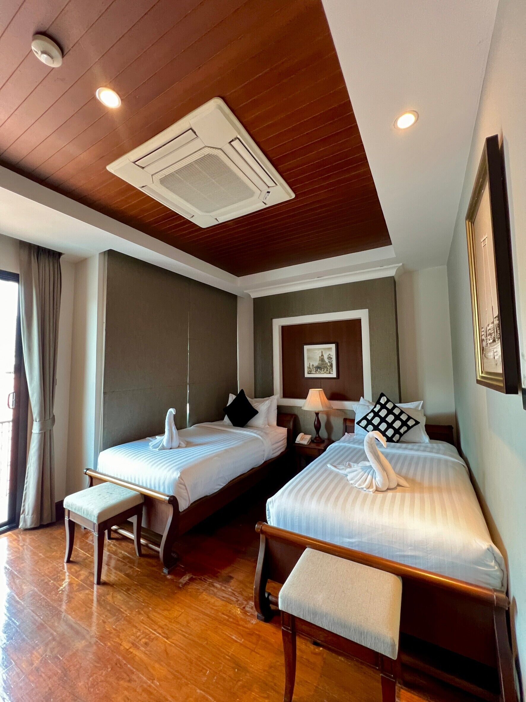 Une chambre d’hôtel avec deux lits, un plancher en bois, un ventilateur de plafond et un tableau encadré au mur.