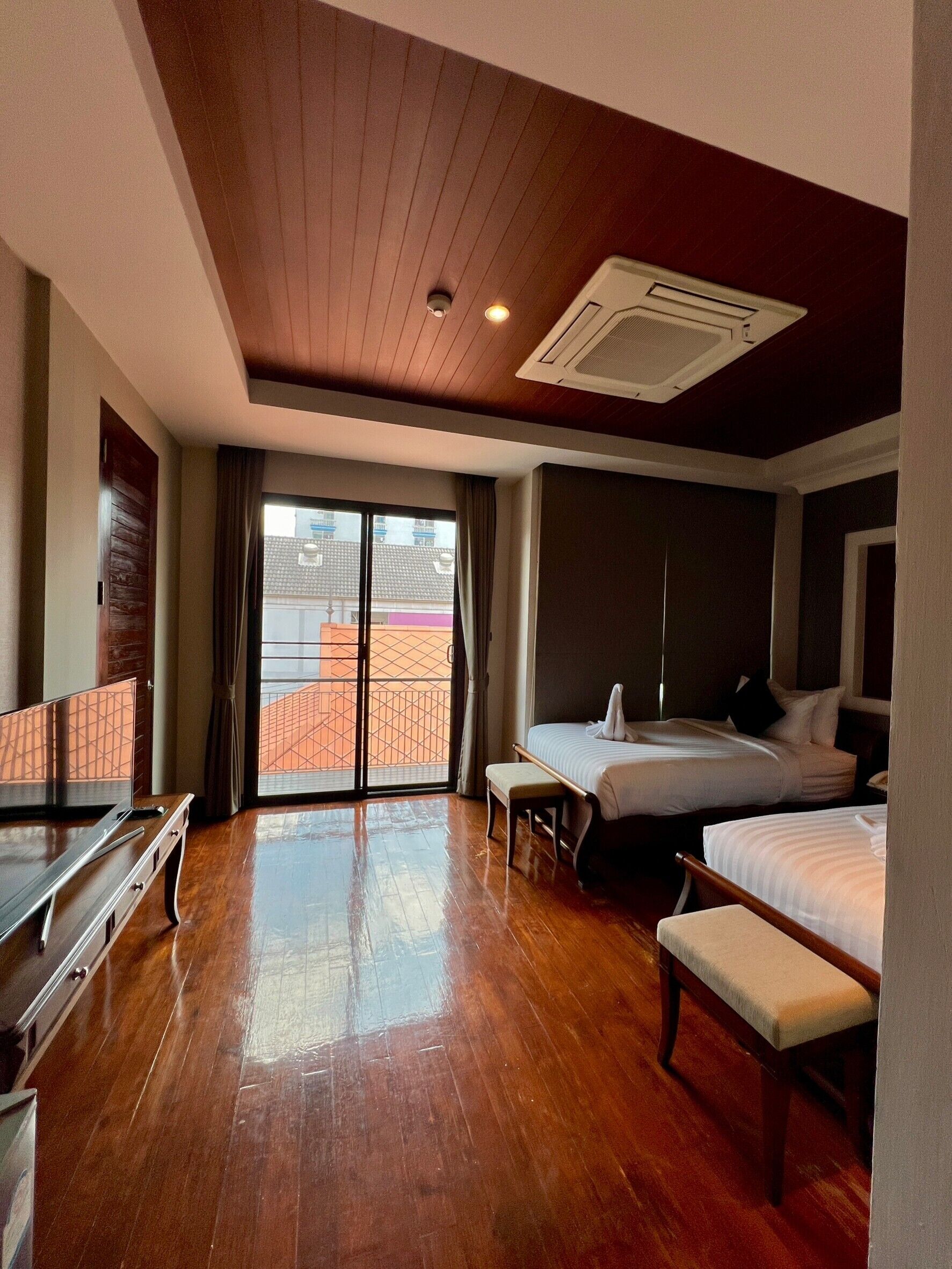 A hotel room with a wooden floor, a bed, a bench, a desk, and a sliding glass door to the outside.