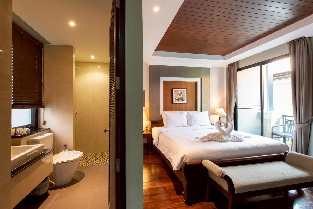 A hotel room with a bed, bedside table, and a bathroom with a sink and toilet.