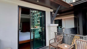 A balcony with wooden furniture, a sliding glass door leading to a room with a bed, and a view of the sky. - Yotaka Bangkok Hotel (Bangkok)