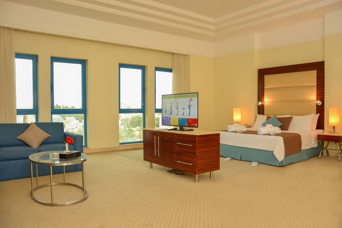 A hotel room with a bed, a desk, a chair, a TV, and a sofa.