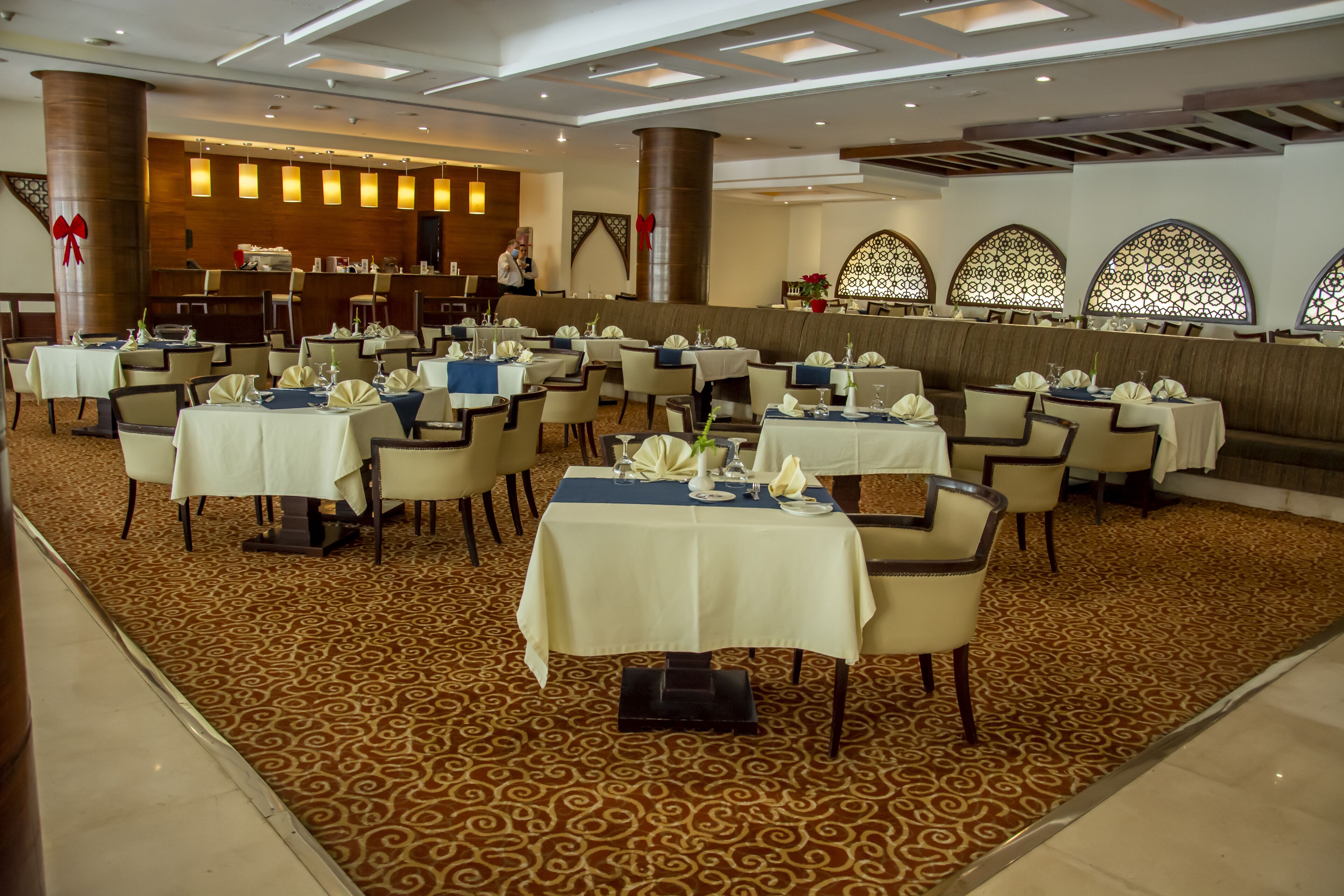 Un salón de banquetes con varias mesas redondas, cada una con mantel blanco y sillas, y una alfombra estampada.