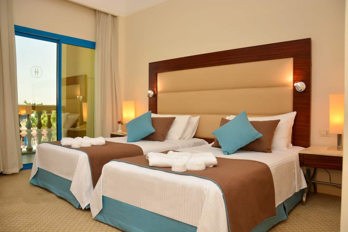 A hotel room with two beds, a balcony, and a view of the city.