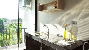 A modern kitchen with a large window, a built-in sink, and a wooden shelf above it. - The Vert Apartment (Bangkok)