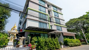A multi-story hotel with a modern design, featuring a prominent entrance with a covered walkway and lush greenery in front. - The Vert Apartment (Bangkok)