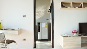 A modern room with a built-in refrigerator, a desk with a computer, a chair, and a shelf with books. - The Vert Apartment (Bangkok)