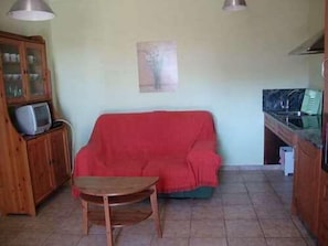 A compact living space with a red sofa, a wooden cabinet with a television, and a small table.