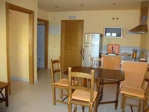 A dining area with a wooden table and chairs, a refrigerator, and a television on the wall.