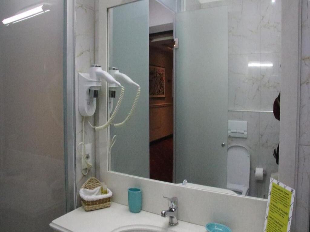 Un baño con un lavabo blanco, un espejo, un secador de pelo y un cesto para toallas.
