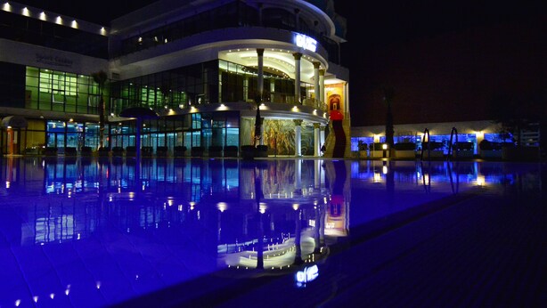 A multi-story hotel with a pool in front, featuring a large glass facade and illuminated signage. - Te Stela Resort (Kashar)