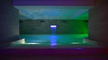 A modern indoor pool with a central waterfall feature, surrounded by wooden walls and a ceiling with a geometric design.
