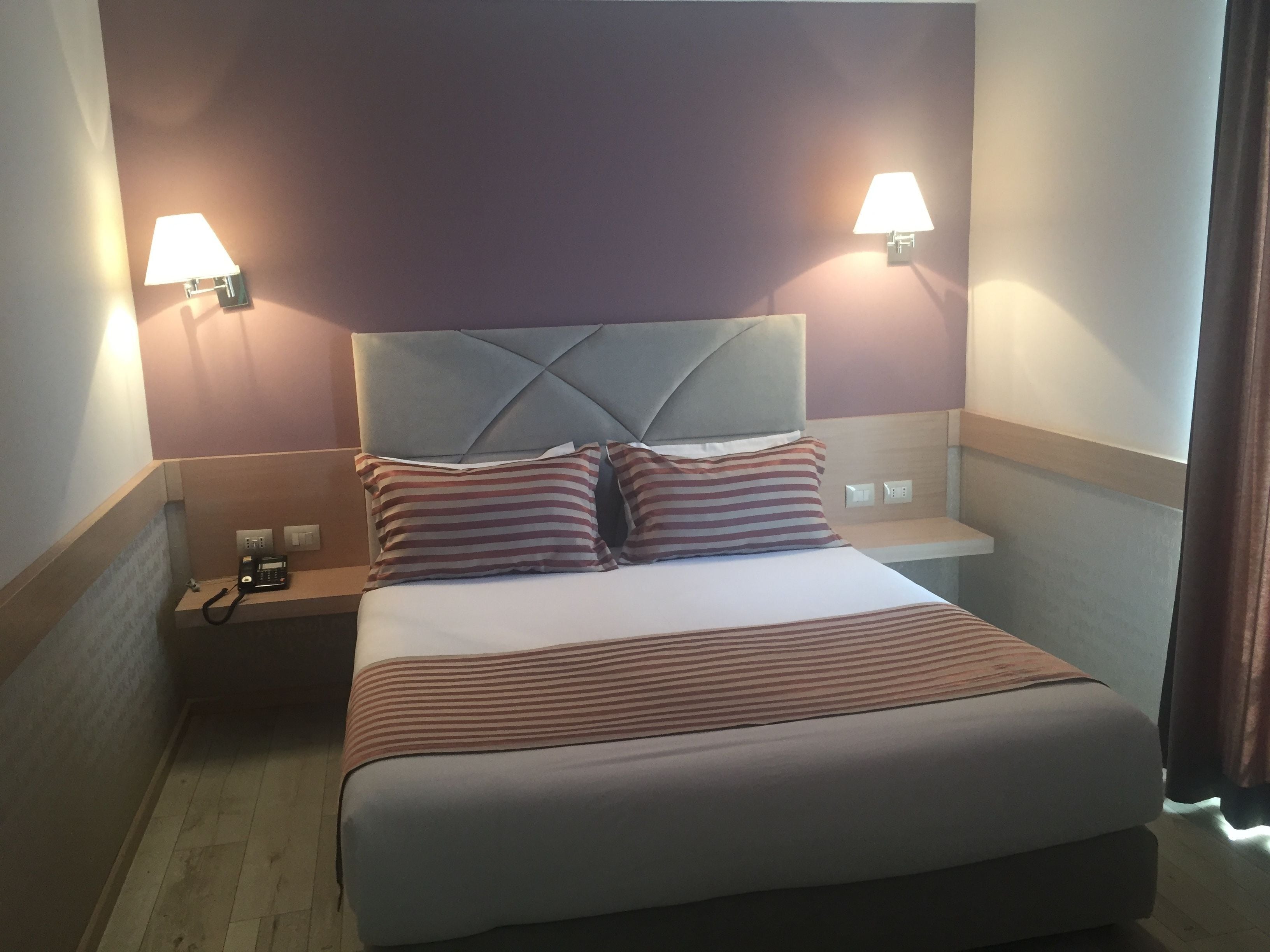 A hotel room with a bed, two bedside lamps, a telephone, and a nightstand.