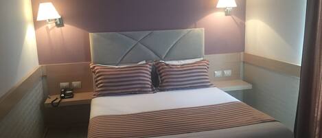 A hotel room with a bed, two bedside lamps, a telephone, and a nightstand.