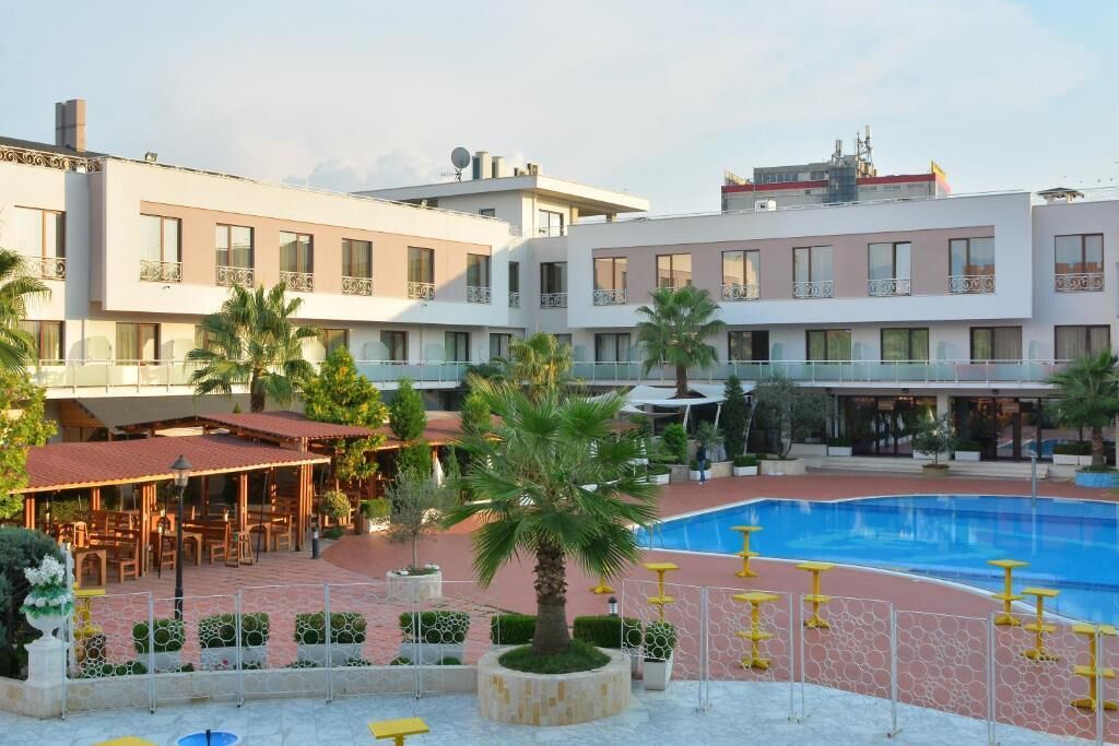 A hotel with a swimming pool, outdoor seating, and a courtyard with palm trees.