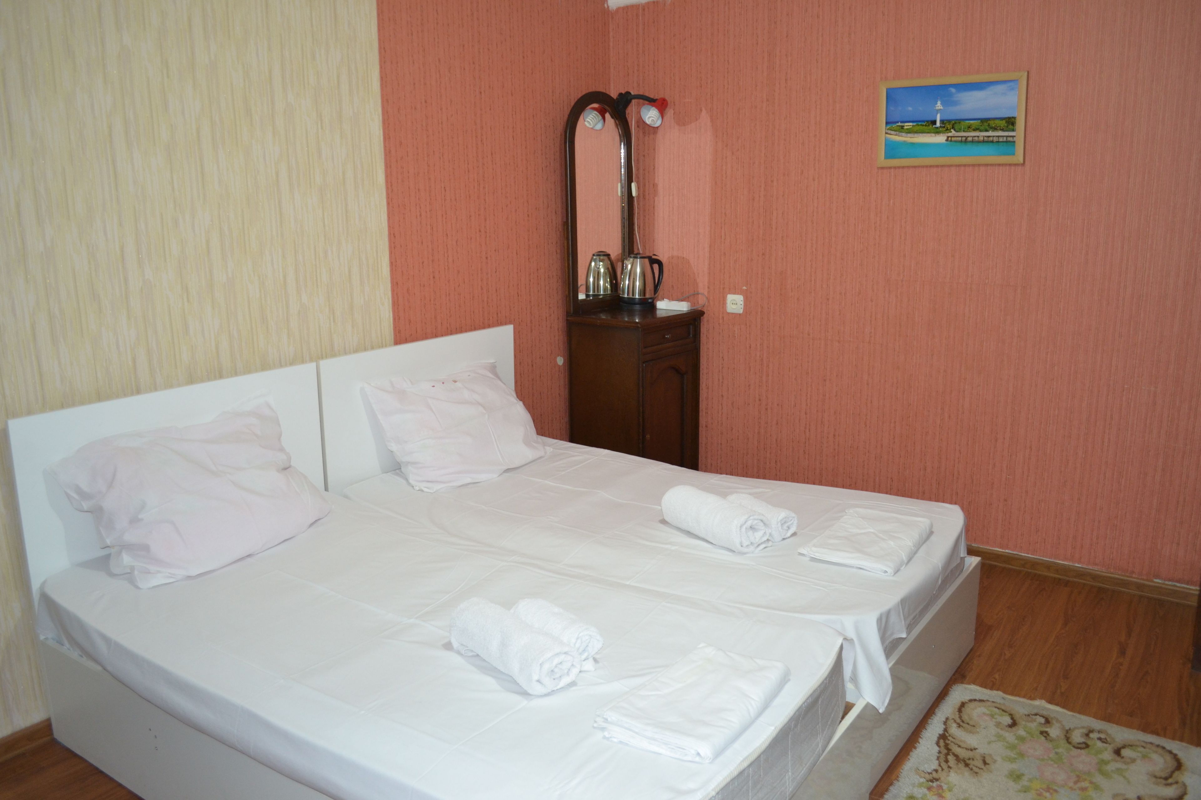 A double bed with white linens, a wooden nightstand with a mirror and two lamps, and a small framed picture on the wall.
