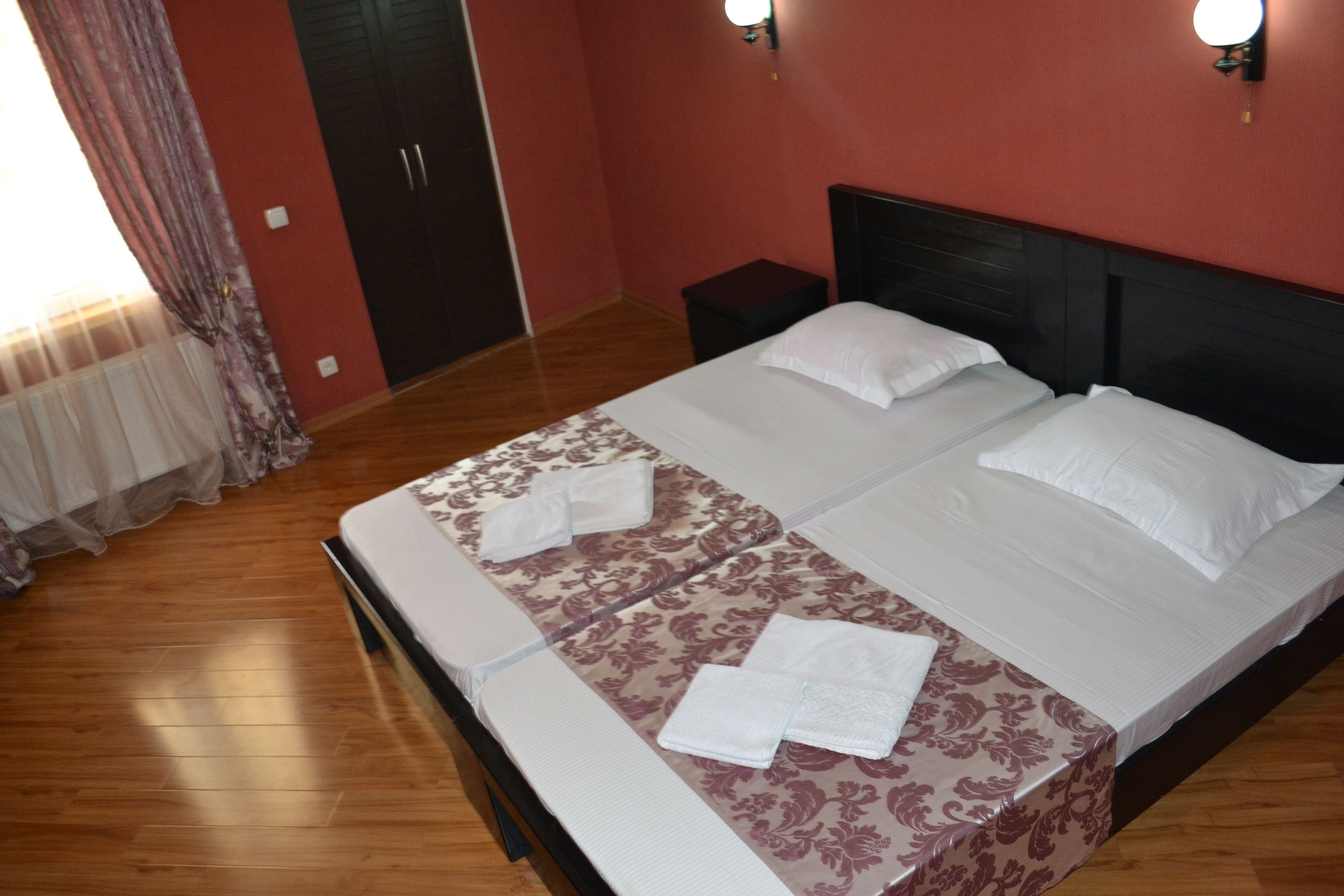 A double bed with a patterned bedspread and two pillows, a nightstand, a wardrobe, and a window with curtains.
