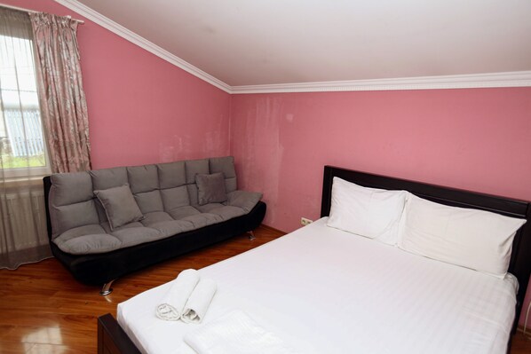 A bedroom with a bed, a grey sofa, and a window with curtains.