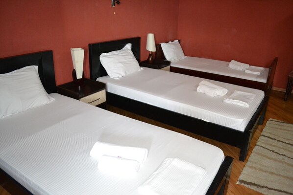 A hotel room with three single beds, each with white linens and pillows, wooden headboards, and bedside tables with lamps. - Hotel Isaka (Tbilisi)